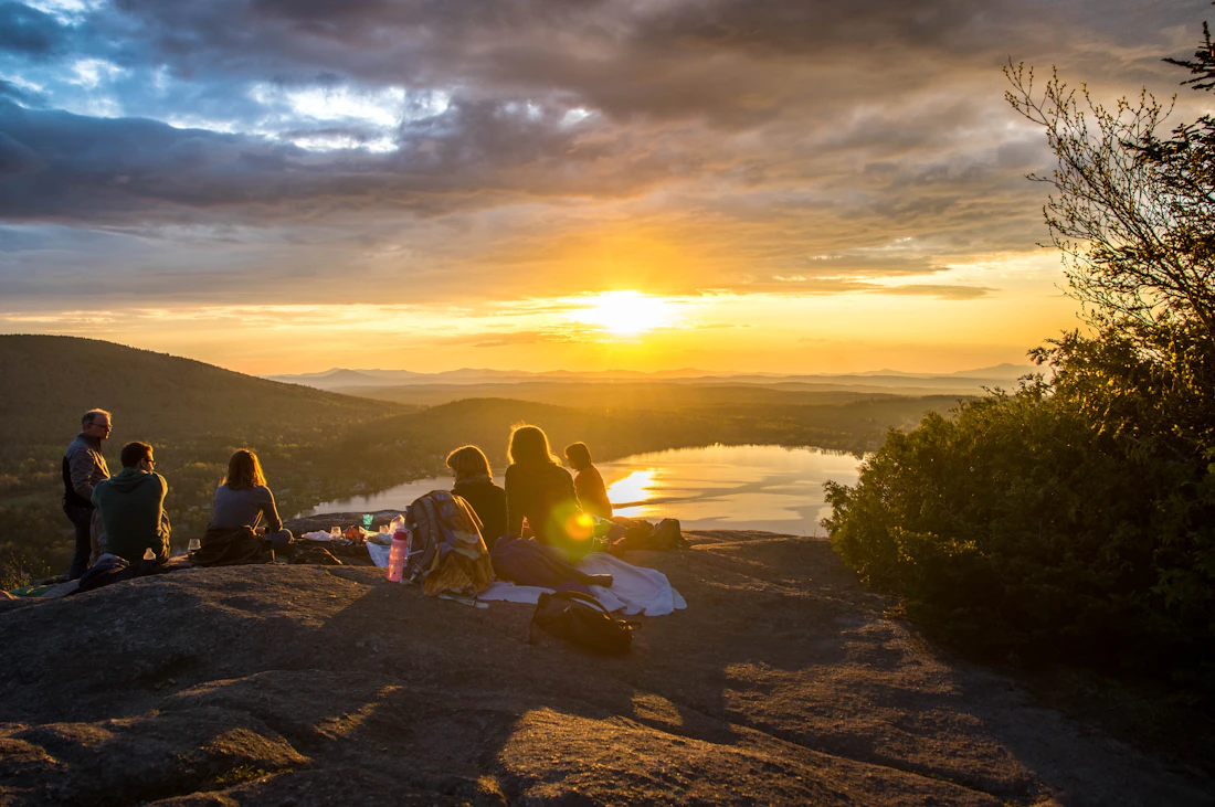 Amis assis sur un rocher face au coucher du soleil sur un lac
